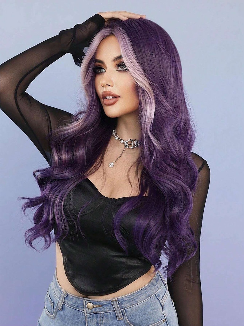 May include: A woman with long, wavy purple hair with a light blonde face-framing highlight. She is wearing a black satin top, a sheer black long-sleeved shirt, and blue jeans. A silver necklace with a pendant is around her neck.