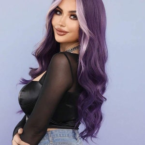 May include: A long, wavy purple wig with a light purple face-framing highlight. The wig is 28 inches long. The model is wearing a black top and blue jeans. The background is a light blue.
