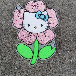 May include: A pink flower with glitter, featuring a white Hello Kitty character with a blue bow. The flower has green leaves and a stem.