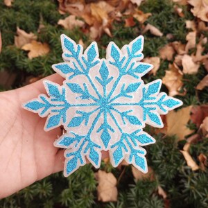 May include: A white snowflake ornament with blue glitter. The snowflake is 3D and has a detailed design.