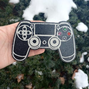 May include: A black and white PlayStation controller with a textured surface. The controller has a white outline and colored buttons.