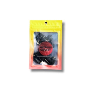 May include: A clear plastic bag with a gradient yellow to pink background, containing several small black hair rollers. A red circular sticker with the text "THE SMART CARPET" is visible inside the bag.