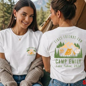 Peut inclure: Un t-shirt blanc avec un petit motif sur la poitrine gauche et un grand motif au dos. Les illustrations incluent des pins verts, une tente jaune, un camping-car et le texte "FIRES FRIENDS FUN CAMP EMILY Lake Tahoe, 2026".