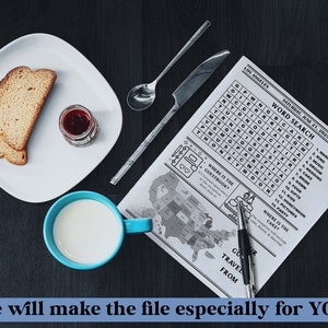 May include: A black and white word search puzzle with the title "Word Search" and the date "Saturday, June 21, 2025". The puzzle is on a white sheet of paper with a map of the United States in the background. There is a blue cup with milk, a plate with two slices of bread, a small jar of jam, and a silver spoon on a dark wooden surface.