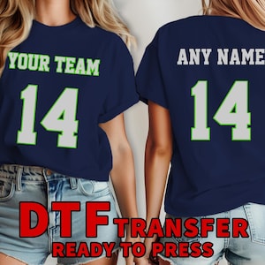 Puede incluir: Una camiseta azul marino con un número blanco "14" y un contorno verde. El texto "YOUR TEAM" está impreso encima del número. La camiseta está lista para ser presionada con un diseño de transferencia térmica.