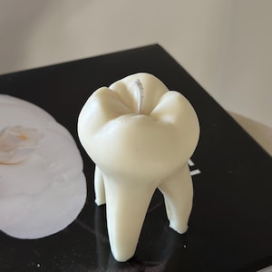 May include: A white tooth-shaped candle with a white wick. The candle is sitting on a black surface.