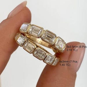 May include: Two gold rings with emerald-cut diamonds. The top ring has 6 diamonds, each 5x3.5mm, totaling 2.10 TC. The bottom ring has 7 diamonds, each 4x3mm, totaling 1.40 TC. The rings are held by a person.