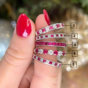 May include: Five silver rings with various gemstone arrangements. The rings feature alternating white and red gemstones, and some have a continuous line of red stones. The gemstones are set in a silver band.