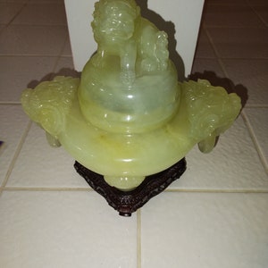 May include: A green jade incense burner with a lion finial and three dragon handles. The burner is sitting on a wooden base.