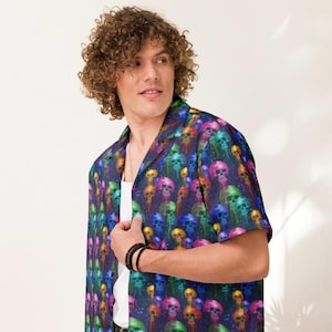 May include: A short-sleeved button-down shirt featuring a vibrant, all-over print of colorful skulls. The skulls are depicted in shades of pink, blue, green, and yellow against a dark blue background. The shirt has a classic collar and a relaxed fit.