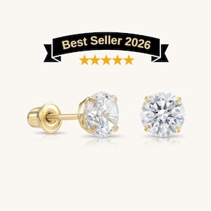 May include: A pair of gold stud earrings featuring round, clear, faceted stones held by four-prong settings. The earrings include threaded posts and screw-on backs. Above the earrings is a black banner with the text Best Seller 2026 and five stars.
