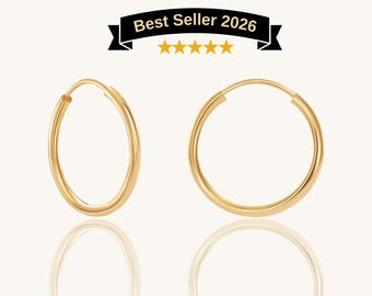 May include: A pair of gold hoop earrings with a smooth, polished finish. Above the earrings, a black banner displays the text Best Seller 2026 with five yellow stars underneath. The earrings are circular with a thin wire closure mechanism.