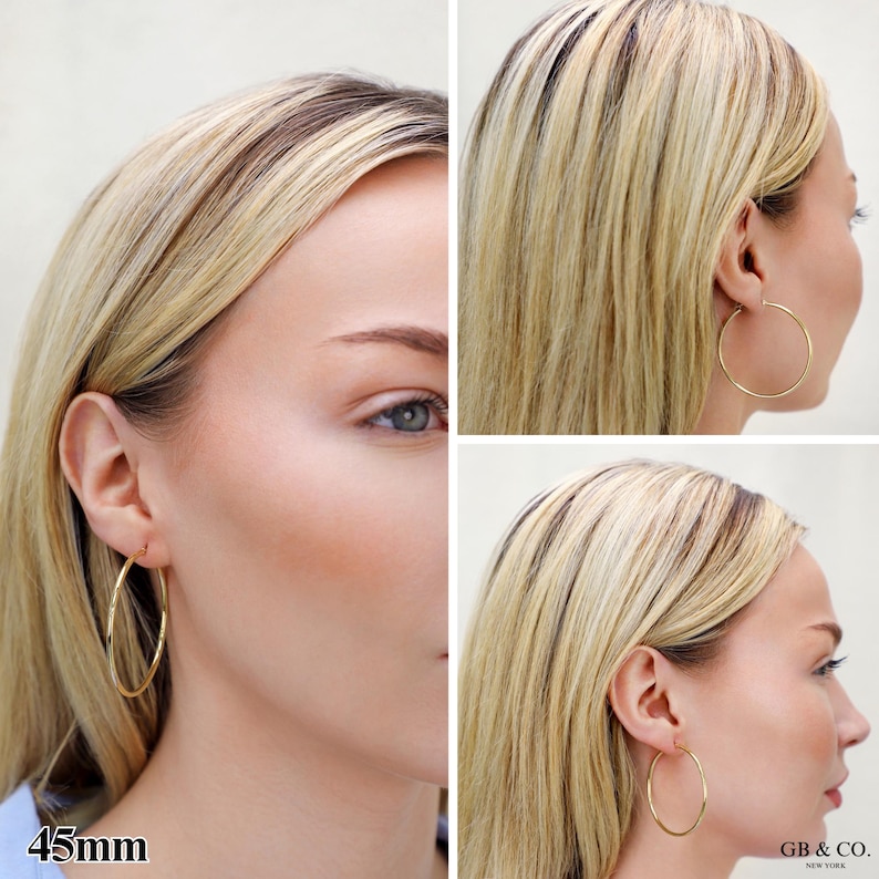 May include: A pair of thin gold hoop earrings with a 45mm diameter. The earrings feature a simple, circular wire design that loops through the earlobe. The text 45mm is visible in the bottom left corner and GB & CO. NEW YORK in the bottom right.
