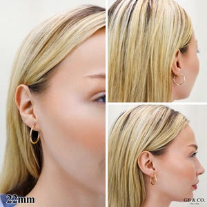 May include: A pair of gold hoop earrings with a smooth, polished finish. The earrings are circular in shape and feature a thin, lightweight design. The text 22mm is visible in the bottom left corner, and the text GB & CO. NEW YORK is in the bottom right.