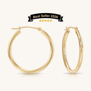 May include: Two gold-colored hoop earrings. The earrings are round with a smooth, polished surface. The image includes a banner that reads "Best Seller 2026" with five gold stars.