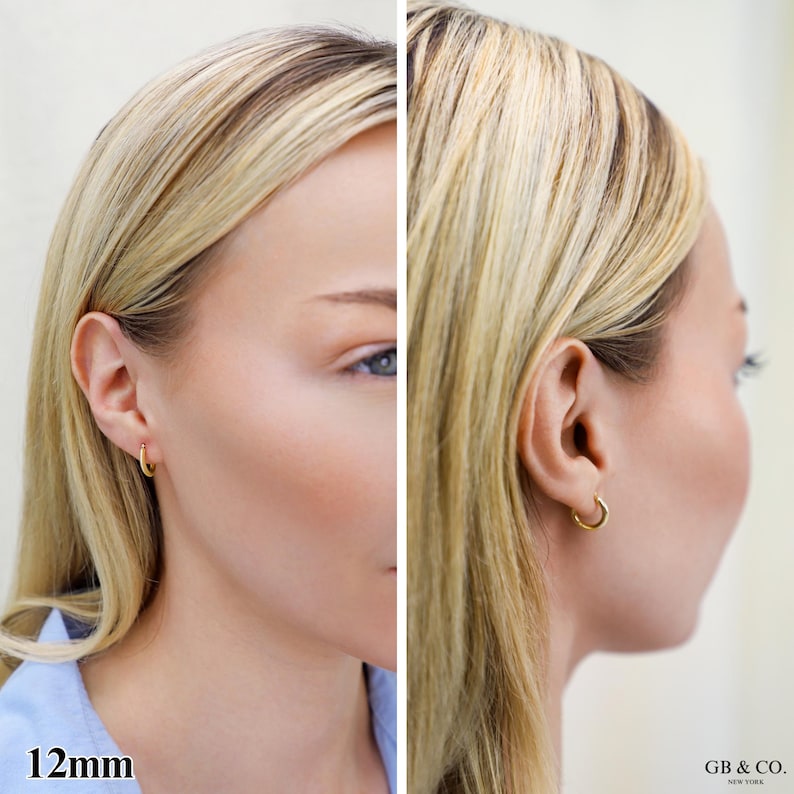 May include: A small gold hoop earring with a 12mm diameter. The earring features a simple, circular design that rests securely in the earlobe. The metal has a polished finish, reflecting light evenly across its smooth, rounded surface.