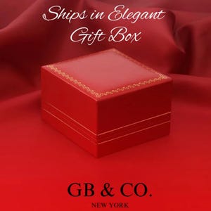 May include: A square red jewelry box with a gold-colored decorative border along the top edge. The text "Ships in Elegant Gift Box" appears at the top, and the text "GB & CO. NEW YORK" is printed in black at the bottom of the image.