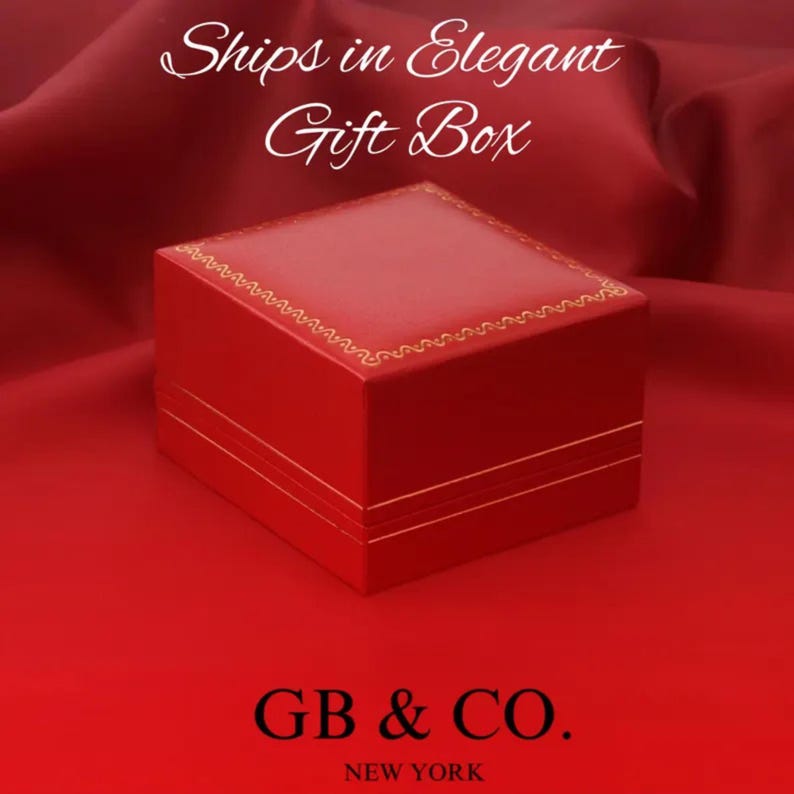 May include: A square red jewelry box with a gold-colored decorative border along the top edge. The text "Ships in Elegant Gift Box" appears at the top, and the text "GB & CO. NEW YORK" is printed in black at the bottom of the image.