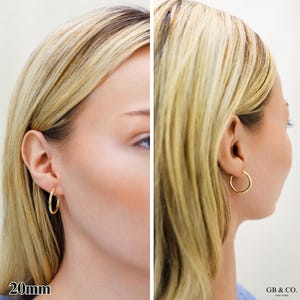 May include: A pair of gold hoop earrings with a smooth, polished finish. The earrings are circular in shape and measure 20mm in diameter. The design is simple and features a thin, continuous metal band that secures through the earlobe.