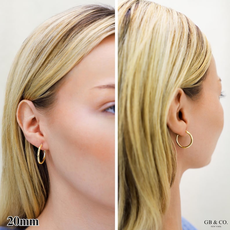 May include: A pair of gold hoop earrings with a smooth, polished finish. The earrings are circular in shape and measure 20mm in diameter. The design is simple and features a thin, continuous metal band that secures through the earlobe.