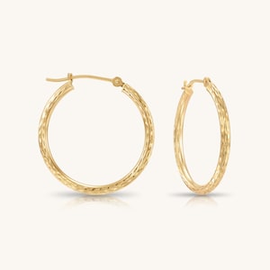 May include: A pair of gold hoop earrings featuring a textured, faceted surface that catches the light. The circular earrings are designed with a hinged post closure mechanism, providing a secure fit. The metal has a warm, polished yellow gold tone.