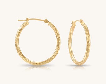 May include: A pair of gold hoop earrings featuring a textured, faceted surface that catches the light. The circular earrings are designed with a hinged post closure mechanism, providing a secure fit. The metal has a warm, polished yellow gold tone.