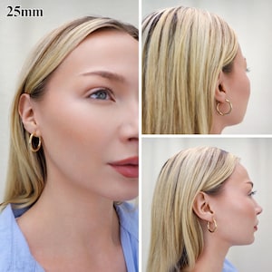May include: A pair of gold-toned hoop earrings with a smooth, polished finish. The circular earrings have a diameter of 25mm as indicated by the text in the upper left corner. The hoops feature a simple, continuous design that secures through the earlobe.