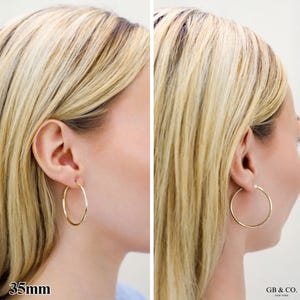 May include: A pair of polished gold hoop earrings with a circular design. The earrings have a diameter of 35mm as indicated by the text. The jewelry features a thin, smooth metal band that forms a complete circle, worn in the earlobe.