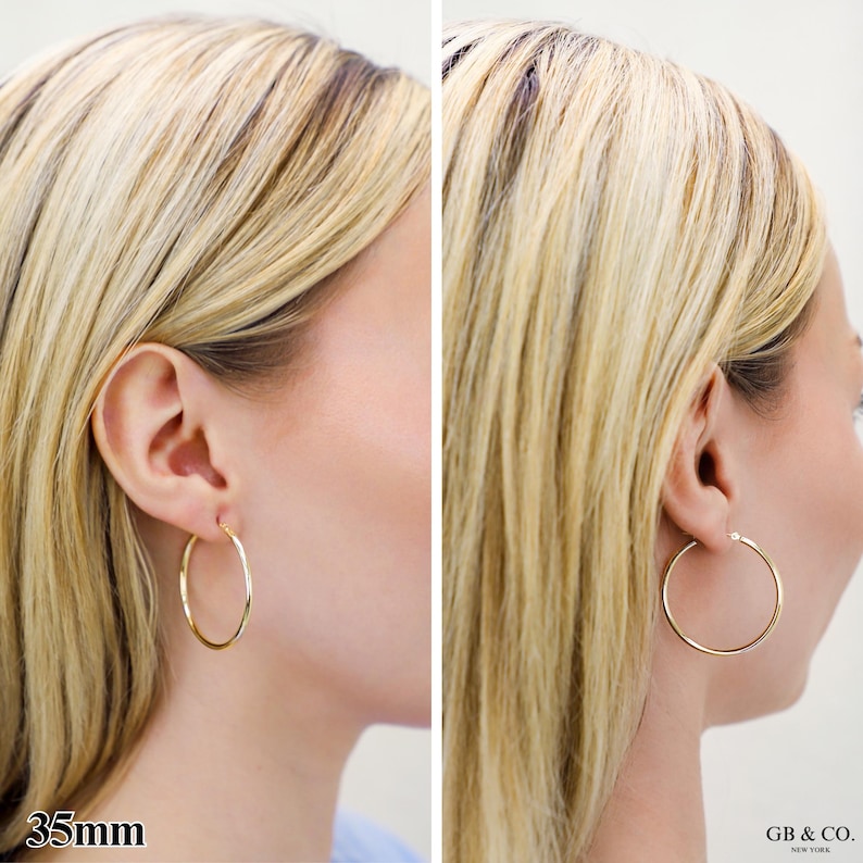 May include: A pair of polished gold hoop earrings with a circular design. The earrings have a diameter of 35mm as indicated by the text. The jewelry features a thin, smooth metal band that forms a complete circle, worn in the earlobe.