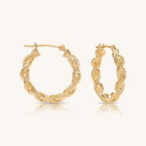May include: A pair of gold hoop earrings featuring a twisted rope design with a textured finish. The earrings are circular in shape and include a hinged post closure mechanism at the top, showcasing a polished metallic surface throughout the piece.