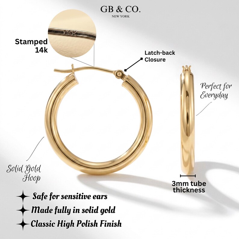 May include: A pair of polished solid gold hoop earrings featuring a latch-back closure. The hoops have a 3mm tube thickness and are stamped 14k. The text GB & CO. NEW YORK is visible at the top, along with labels for the latch-back and 14k stamp.
