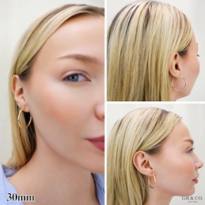 May include: A pair of gold hoop earrings with a 30mm diameter. The earrings are circular, thin, and polished, featuring a simple wire closure. The text 30mm is visible in the bottom left corner, and the brand name GB & CO. NEW YORK is in the bottom right.