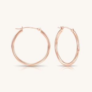 May include: A pair of rose gold hoop earrings with a smooth, polished finish. Each earring features a circular design with a hinged post closure at the top, showcasing a consistent metallic hue and a simple, rounded profile for the hoop structure.