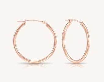 May include: A pair of rose gold hoop earrings with a smooth, polished finish. Each earring features a circular design with a hinged post closure at the top, showcasing a consistent metallic hue and a simple, rounded profile for the hoop structure.