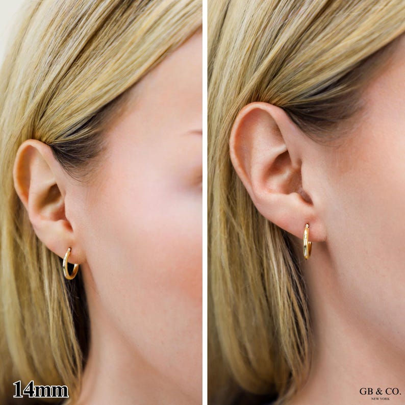 May include: A small, polished gold hoop earring with a 14mm diameter. The earring features a simple, circular design that sits securely in the earlobe. The metal has a smooth, reflective surface, and the piece is branded with GB & CO. NEW YORK.
