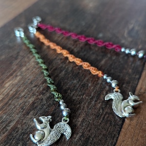 May include: Three handmade braided cord bracelets with silver squirrel charms. The bracelets are green, orange, and red.