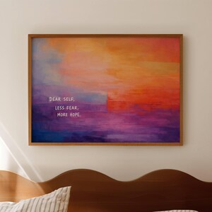 May include: A rectangular framed wall art piece featuring an abstract gradient background transitioning from orange and yellow at the top to purple and blue at the bottom. The text "DEAR SELF, LESS FEAR, MORE HOPE." is printed in white on the left side.