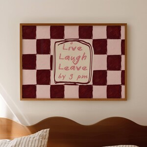 May include: A rectangular wall art print in a wooden frame featuring a dark red and light pink checkered pattern. In the center, a cream-colored square with a hand-drawn border contains the handwritten text: Live Laugh Leave by 9 pm.