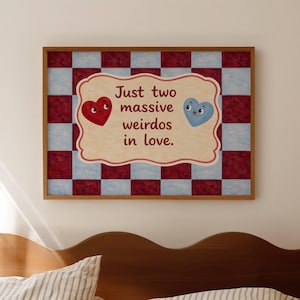 Op de afbeelding: Een ingelijste print met een rood en lichtblauw dambordpatroon. De print heeft een crèmekleurige banner met geschulpte randen met de tekst "Just two massive weirdos in love." Twee cartoonhartjes, één rood en één blauw, zijn ook afgebeeld.