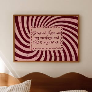 May include: A framed print with a swirling red and white background. The print features the text "Turns out these are my monkeys and this is my circus" in a pink, decorative font. The frame is a warm brown color.
