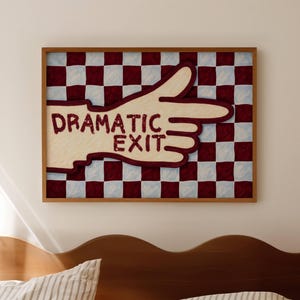 Puede incluir: Una pieza de arte mural rectangular enmarcada que muestra una mano de color crema señalando hacia la derecha, sobre un fondo de cuadros granates y azul claro. El texto "DRAMATIC EXIT" aparece en letras granates en la palma de la mano.