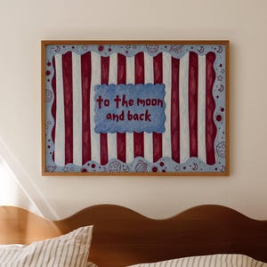 Könnte beinhalten: Ein gerahmtes Kunstwerk mit einem skurrilen Design. Das Kunstwerk hat einen Hintergrund aus abwechselnd roten und weißen vertikalen Streifen. Ein blaues wolkenförmiges Element in der Mitte zeigt den Text "to the moon and back". Der Rahmen hat eine warme braune Farbe.