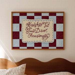 Pode incluir: Uma impressão de arte emoldurada com o texto "Kiss All The Time Disco Occasionally" em um roteiro caprichoso. A obra apresenta um fundo xadrez em bordô e azul claro, com um painel central creme com bordas onduladas.