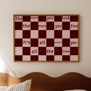Può includere: Una stampa artistica da parete rettangolare in una cornice di legno con un motivo a scacchiera di quadrati marrone scuro e rosa chiaro. Il testo "the more you look the more you find it's all around you all the time" è scritto in nero sui quadrati.