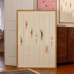 Puede incluir: Tres impresiones artísticas enmarcadas con temática de natación. La impresión más grande presenta nadadores en una piscina con líneas azules. Dos impresiones más pequeñas muestran nadadores sobre fondos rosas y crema. Todas las impresiones tienen marcos de madera.