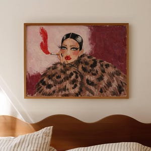 May include: A framed rectangular painting featuring a person with dark hair, bold makeup, and red lips, wearing a brown and black leopard print coat. The person holds a cigarette with a bright red plume of smoke against a pink and maroon background.