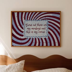 May include: A framed artwork with a swirling red, white, and blue background. The artwork features the text "Turns out these are my monkeys and this is my circus" in a white, scalloped-edged box. The frame is a warm brown color.