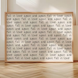 May include: A rectangular framed wall art piece featuring a light beige background with the repeating black handwritten text "fall in love again and again" covering the entire surface in a grid-like pattern, encased in a simple light wood frame.