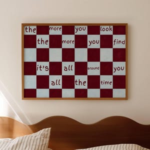 May include: Framed artwork with a checkerboard pattern in burgundy and white. The text "the more you look, the more you find, it's all around you all the time" is displayed in a handwritten style. The frame is a warm brown color.