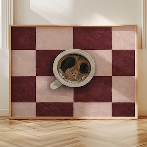 Può includere: Un'opera d'arte incorniciata con una tazza di caffè su una superficie a scacchi. La tazza di caffè è bianca con un manico grigio chiaro, piena di caffè scuro. Il motivo a scacchi alterna quadrati bordeaux e rosa chiaro, il tutto all'interno di una cornice di legno.